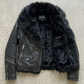Studio flat lay photography of a high-quality black leather jacket with detachable black faux fur collar.