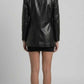 A model shown from the back wearing a black textured croc leather blazer, a short black skirt, and black high heels against a light gray studio background.