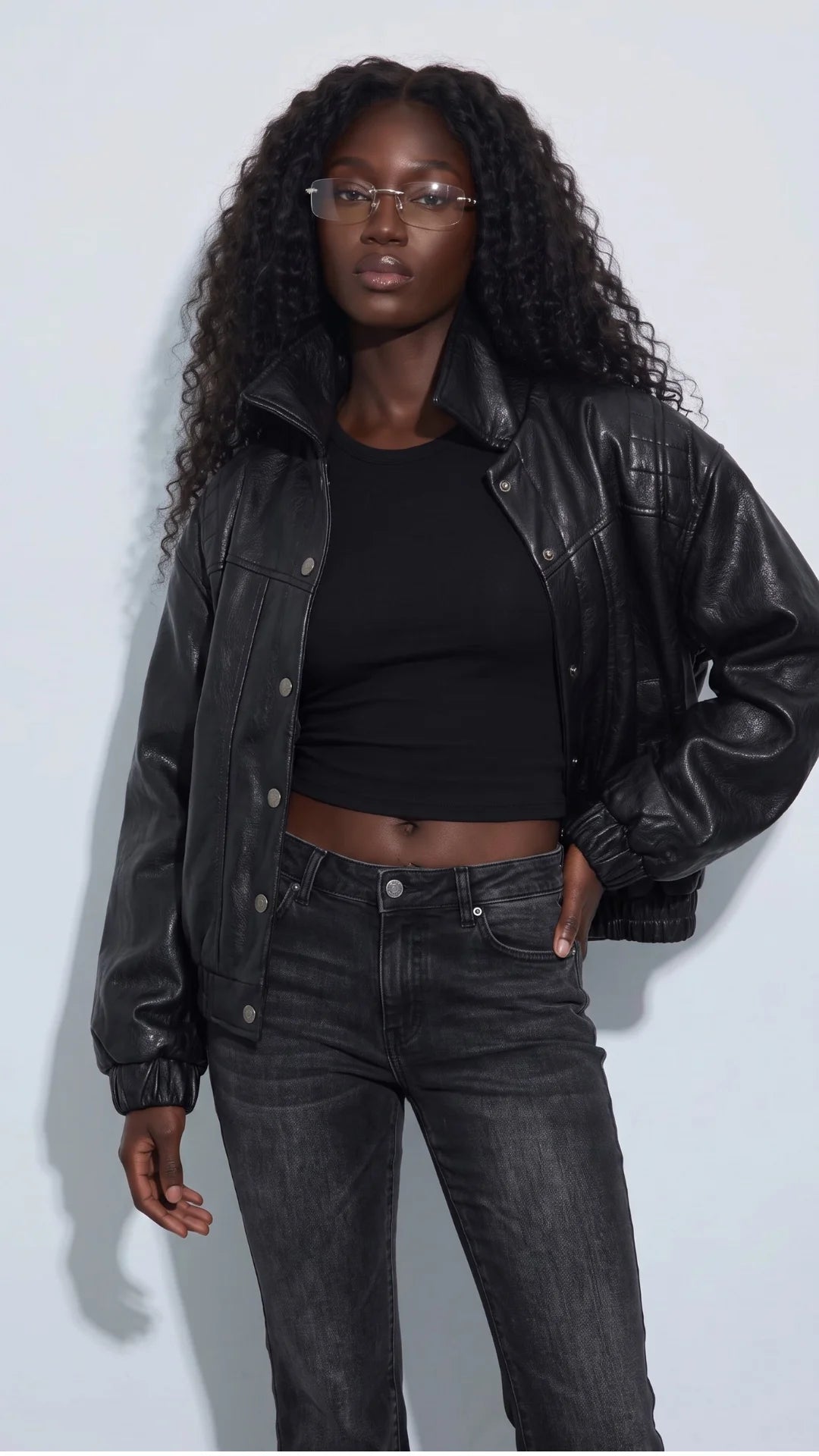 Women’s black genuine leather cropped jacket styled with a fitted black top and washed-black jeans for a confident monochrome streetwear look. Its relaxed shape, glossy leather finish, quilted shoulder panels and silver-tone snap buttons add texture and structure, making this short leather jacket a standout choice for modern city outfits and effortless everyday layering.