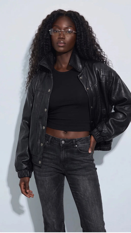 Women’s black genuine leather cropped jacket styled with a fitted black top and washed-black jeans for a confident monochrome streetwear look. Its relaxed shape, glossy leather finish, quilted shoulder panels and silver-tone snap buttons add texture and structure, making this short leather jacket a standout choice for modern city outfits and effortless everyday layering.