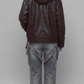 A person shown from the back wearing a JACKERO dark burgundy leather hooded jacket with a dark fur-trimmed hood, paired with faded blue jeans, against a plain light gray studio background.